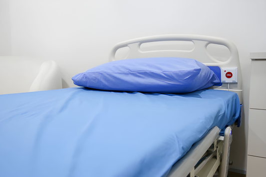 Clean hospital bed with blue sheets and a matching pillow in a clinical room, featuring a white headboard and bedside control panel.